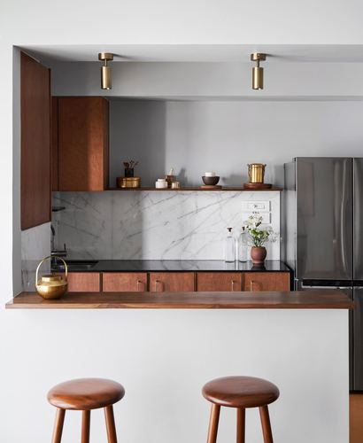 Kitchen with wood cabinetry, marble backsplash, black countertop, brass fixtures, and two wooden bar stools