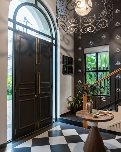 Foyer with arched black door, checkerboard floor, ornate chandelier and staircase