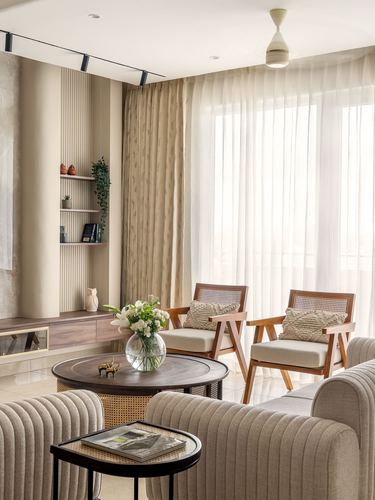 Beige living room with cane armchairs, ribbed sofas, round wooden coffee table and sheer-curtained windows