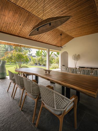 Open-air dining pavilion with live-edge wood table, woven chairs, bamboo ceiling, garden view