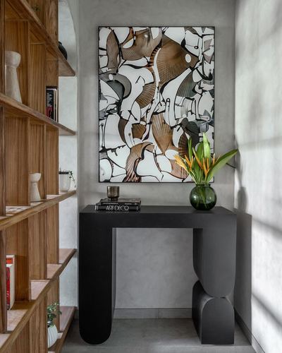 Black sculptural console table under abstract art, beside wooden shelving in textured foyer