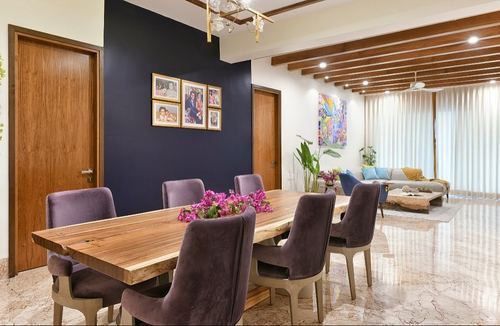 Dining room with live-edge wood table, purple velvet chairs, navy wall with framed photos, living room beyond