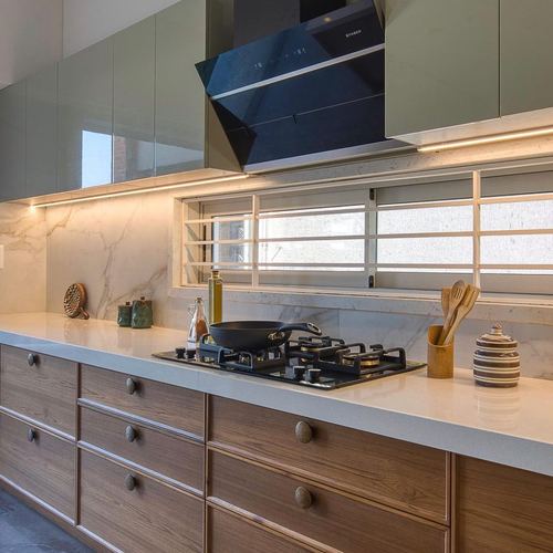 Kitchen counter with black gas hob, veined stone backsplash, wooden drawers and sage upper cabinets