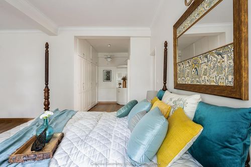 Bedroom with carved wood four-poster bed, teal and yellow pillows, framed mirror above headboard