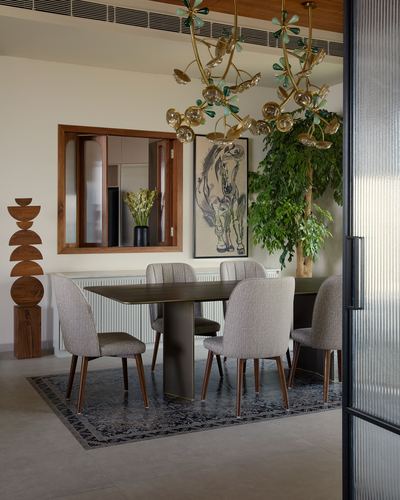 Dining room with brass floral chandelier, upholstered chairs, dark wood table, and large indoor tree.