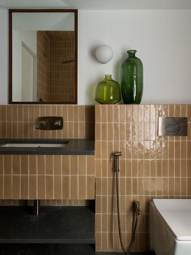Terracotta tiled bathroom with dark stone counter, brass fittings and green glass vases on ledge