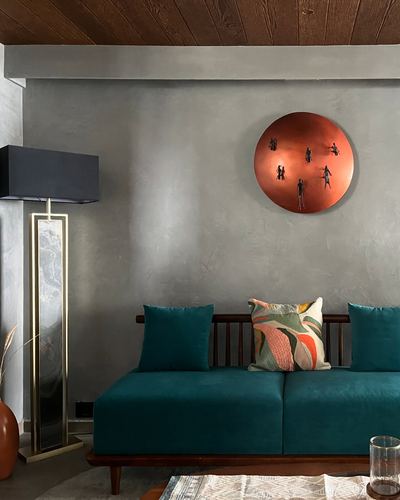 Teal velvet sofa against lime plaster wall with circular copper sculpture and wooden ceiling