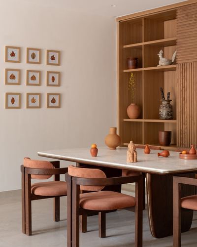 Dining table with terracotta decor beneath open wood shelving and framed leaf prints on a cream wall