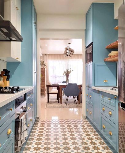 Blue galley kitchen with patterned floor tiles opening to a sunlit dining area
