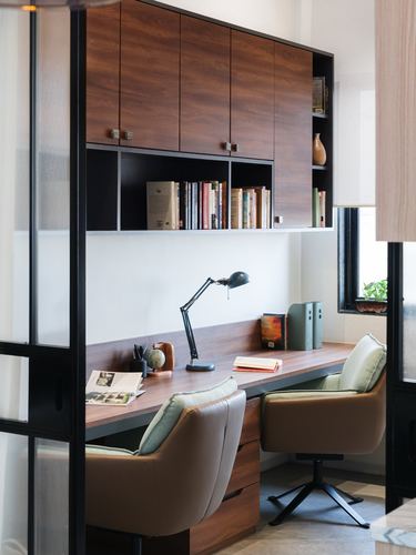 Home study nook with wood cabinetry, desk, lamp and two leather chairs seen through glass partition