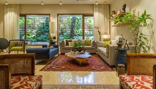 Living room with cane chairs, patterned rug, and large wooden windows opening to a green garden