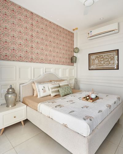 Bedroom with upholstered bed, floral fabric wall panels, and white wainscoting in Vadodara home