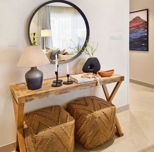 Wooden console table with mirror, lamp, and jute poufs in an entryway