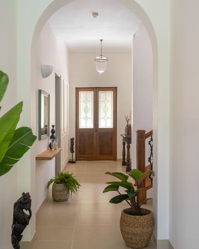 Arched hallway leading to a wooden double door with stained glass, staircase and plants along the way