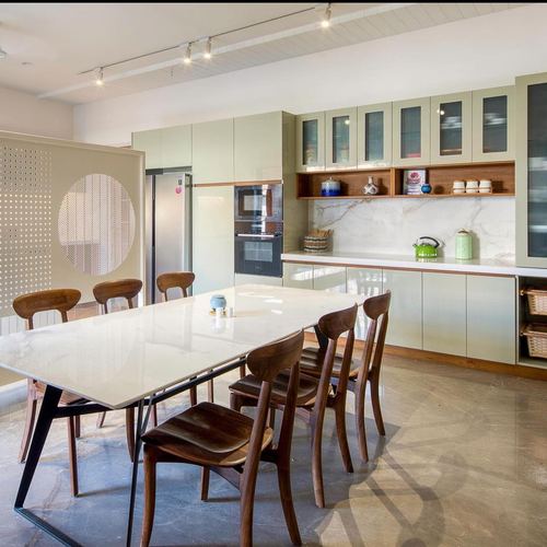 Pastel green kitchen with marble backsplash and wooden dining table with chairs in foreground