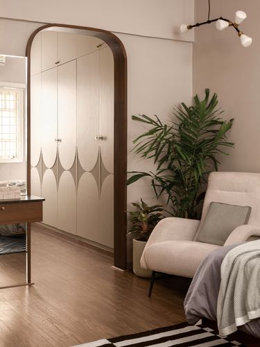 Arched wooden doorway framing a carved wardrobe beside a bedroom with armchair and plants