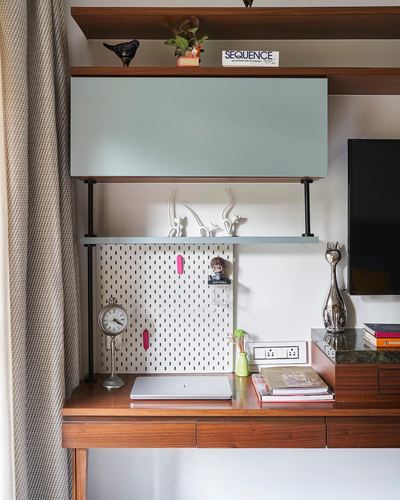 Wooden study nook with floating sage cabinet, pegboard shelf, clock, laptop and cat figurines beside a TV console