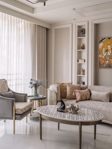 Beige living room with paneled walls, thangka painting, sheer curtains, and oval patterned coffee table