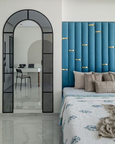 Bedroom with arched black-framed mirror and teal channel-tufted headboard with brass rings