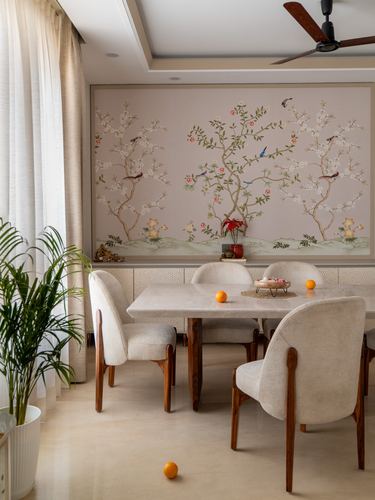 Dining table with cane-back chairs beneath a chinoiserie mural, curtained window and plant beside.
