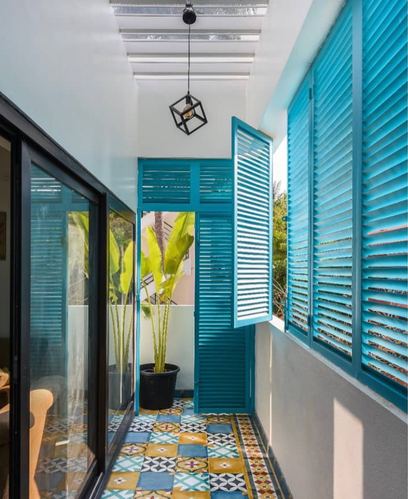 Narrow balcony with turquoise louvered shutters, patterned cement tile floor, and a potted plant