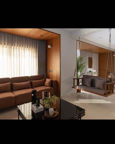 Living room with brown sofa, wood-panelled niche, and a hanging wooden swing bench in adjoining space