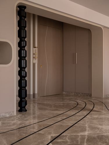 Foyer with sculptural black column, wave-patterned wood door, and inlaid marble flooring with curved black lines