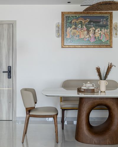 Dining nook with marble-top table, sculptural wood base, and framed Rajasthani miniature painting above