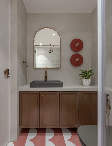 Bathroom vanity with arched mirror, stone basin, wood cabinets, and red patterned floor