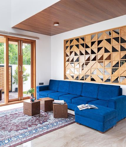 Living room with blue sectional sofa, patterned rug, and geometric wood-mirror panel wall