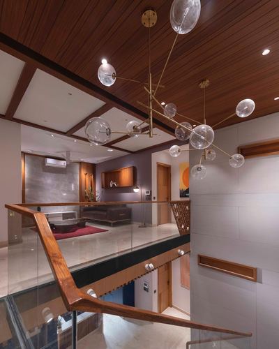 Double-height stairwell with wood-panelled ceiling, glass balustrade with wood handrail, and bubble chandelier overlooking living room below.