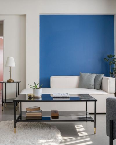 White sofa against a cobalt blue accent wall with black glass coffee table in a minimalist living room