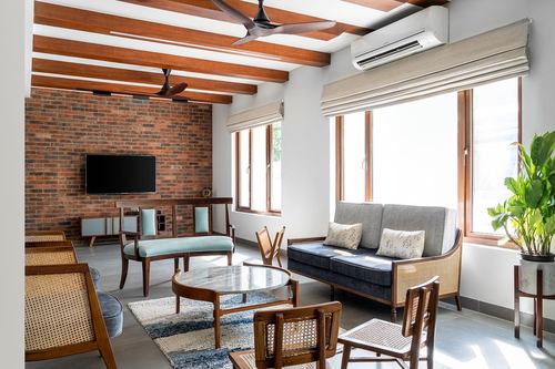 Living room with exposed brick wall, wood beam ceiling, cane chairs, and blue sofa near windows