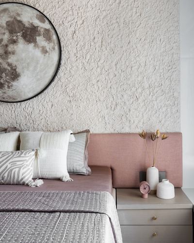 Bedroom corner with textured plaster wall, round moon art, pink headboard and layered pastel cushions