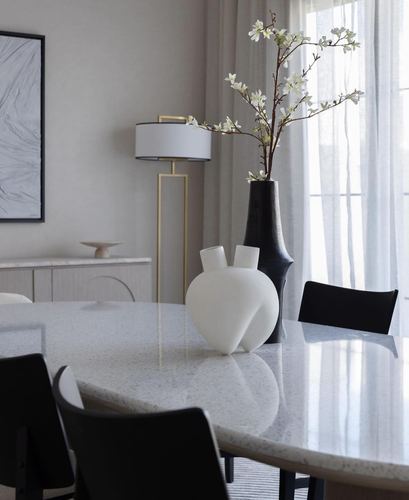 Terrazzo dining table with black chairs, sculptural vases, and a brass floor lamp near sheer curtains