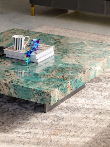 Close-up of a green stone coffee table with mug, books and orchid on a patterned rug