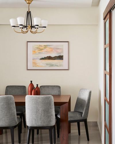 Dining room with wooden table, grey upholstered chairs, chandelier, and framed seascape painting above terracotta vases