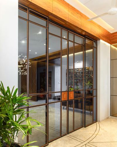 Black metal-framed glass sliding doors under a wood-clad ceiling open to a warmly lit interior room
