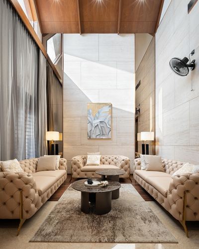 Double-height living room with beige tufted sofas around round coffee tables under a stone feature wall