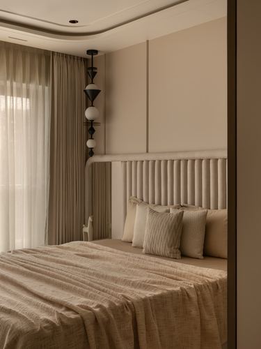 Beige bedroom with tufted headboard, layered bedding, sheer curtains and a black geometric pendant light