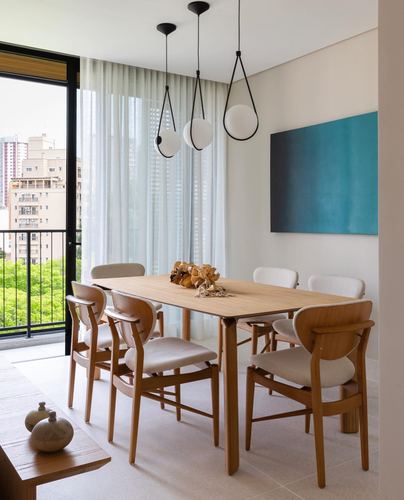 Wooden dining table with cane-back chairs beneath three sculptural pendant lights near sheer curtained window