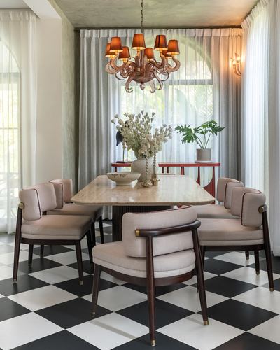 Dining room with marble table, cane-backed chairs, checkerboard floor, and tentacled chandelier under arched window