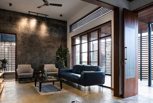 Living room with navy leather sofa, patterned armchairs, stone floor, and slatted wood doors opening to garden