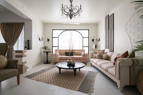 Living room with arched black-framed window, wrought iron chandelier, blush and cream sofas, patterned rug
