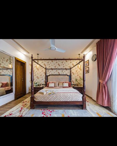 Four-poster wooden bed against floral wallpaper with pink velvet curtains and pendant lights