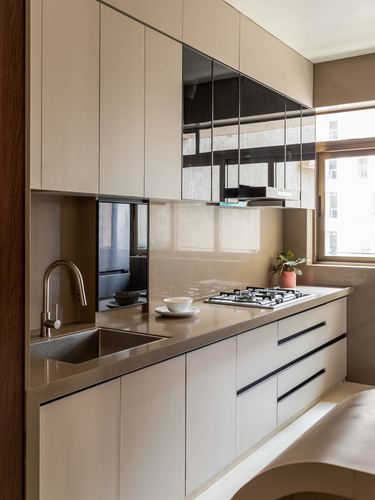 Galley kitchen with beige cabinetry, mirrored backsplash, stone counter, gas hob and sink