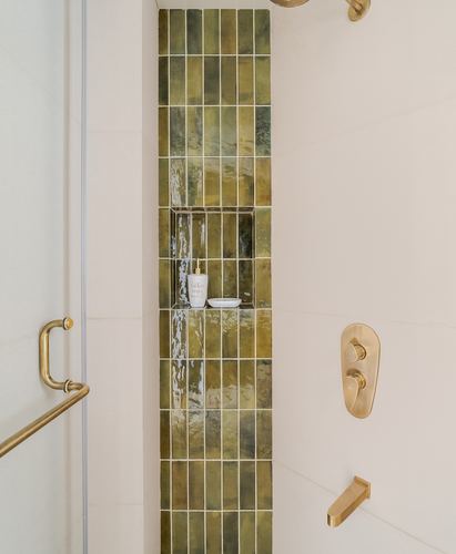 Vertical hand-glazed olive tile shower niche with brass fittings against cream plaster wall