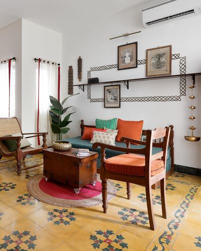 Living room with wooden settee, orange cushions, patterned cement tile floor and wall-mounted family photographs