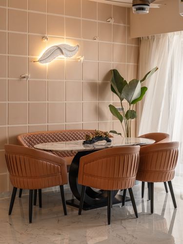 Dining nook with curved tan leather banquette, marble table, and leaf-shaped wall light against pink grid wall