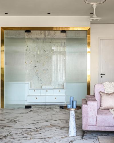 Living room with brass-framed fluted glass wall, marble floor, and pink velvet armchair